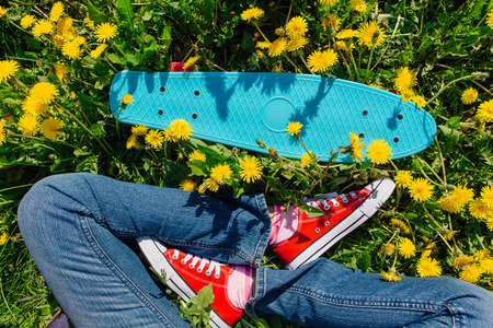Bright and colorful skateboard and female feet in red sneakers on the grassの写真素材