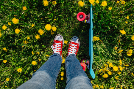 Bright and colorful skateboard and female feet in red sneakers on the grassの写真素材