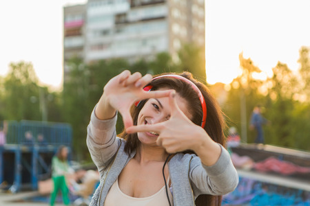 Girl listening to music streaming with headphones shows a frame with fingers.