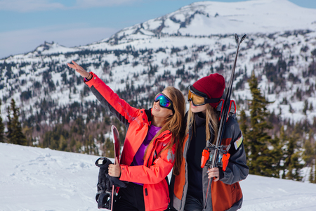 Two young women with ski and snowboard on ski holiday in mountainsの写真素材