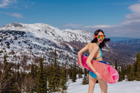 Attractive young woman dressed in swimsuit with snowboard on the slopeの写真素材