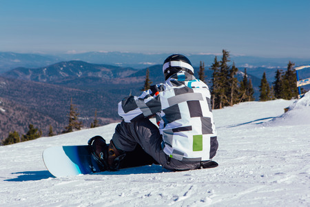 Snowboarder seats on the top of mountain preparing to ride.の写真素材