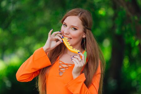Portrait of pretty red hair woman holding juicy delicious orange at summer green park.の写真素材