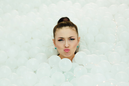Happy beautiful woman lays surrounded by white plastic balls in the dry pool for adult.の写真素材