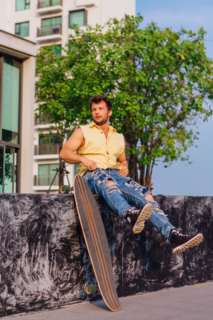 Young handsome man with beard sitting with longboard on the street.の写真素材
