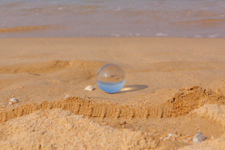 Crystal lens ball lays on the sand beach with seashell