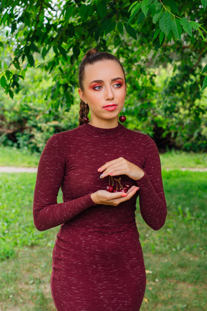 Beautiful young woman with long braid and cherry earrings holding cherry in hands
