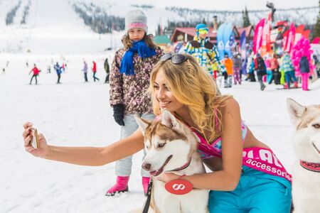 Young happy pretty women in snowboard pants and colorful bikini with Siberian husky dogs on the slopeのeditorial素材