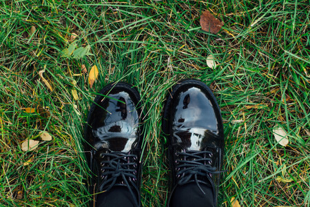 Two feet in black lackered shoes stepping on the green grass with fallen autumn leaves.の写真素材