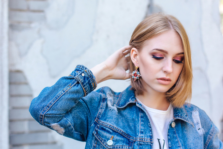 Fashion girl standing near brick wall in denim oversized jacket and beautiful ear rings.の写真素材