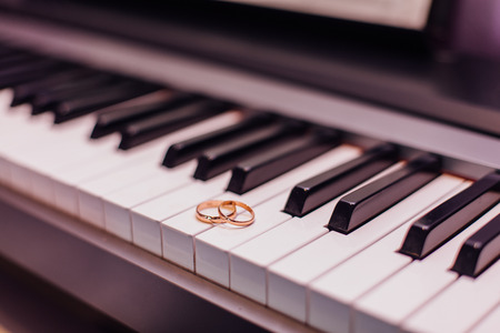 Two golden wedding rings laying on the piano keysの写真素材