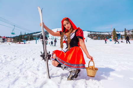 Beautiful young woman in a costume of Little Red Riding Hood with wicker basket and kruasan on the snowy winter slopeの写真素材