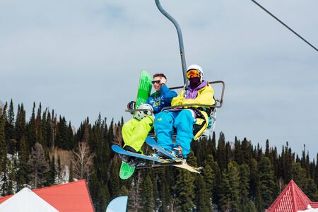 Sheregesh, Mountain Shoria, Kemerovo Region, Russia - April 6, 2018 : Snowboarder and mountain ski rider on a ski lift in ski resortのeditorial素材