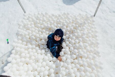 Sheregesh, Kemerovo region, Russia - April 06, 2018 : Happy little boy lays surrounded by white plastic balls in the dry pool outdoors.のeditorial素材