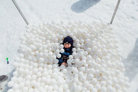 Sheregesh, Kemerovo region, Russia - April 06, 2018 : Happy little boy lays surrounded by white plastic balls in the dry pool outdoors.のeditorial素材