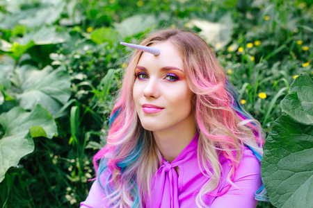 Fairy girl unicorn with rainbow hair and shiny makeup sitting on the grass in the forest.の写真素材