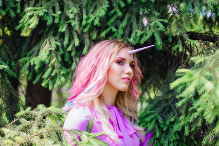 Fairy girl unicorn with rainbow hair and shiny makeup in forest.