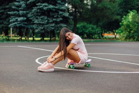Portrait of a smiling charming brunette female sitting on her skateboard on a basketball court.の写真素材