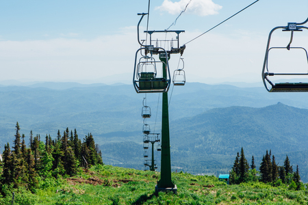 Empty chairs of ski lift at summer time on the background of clear blue sky and green forestの写真素材