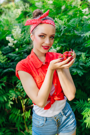 Beautiful young pin up girl dressed in red shirt with bright make up and fresh natural strawberry.の写真素材