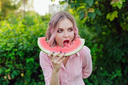 Beautiful young woman with pink hair enjoying sweet juicy watermelonの写真素材