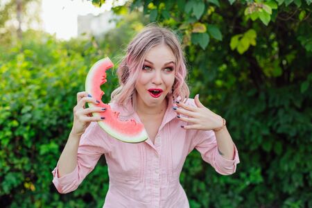 Beautiful emotional young woman with pink hair holding sweet juicy watermelon like telephoneの写真素材