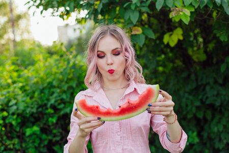 Beautiful young emotional woman with pink hair enjoying sweet juicy watermelonの写真素材