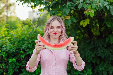 Beautiful young emotional woman with pink hair enjoying sweet juicy watermelonの写真素材