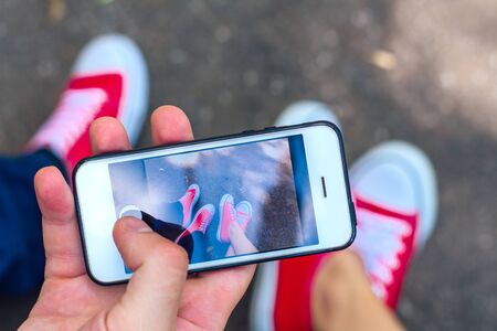 Taking photo with mobile phone of red sneakers shoes on woman's and man's feet. Sneakers shoes...
