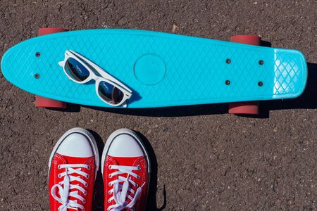 Close up of feet of a girl in red sneakers and mirror sunglasses on a blue penny skate board with pink wheels on the background. Urban scene, city life. Sport, fitness lifestyle.の写真素材
