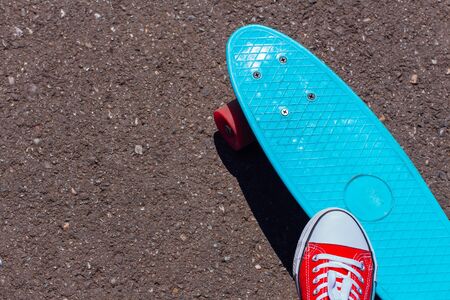 Close up of feet of a girl in red sneakers and blue penny skate board with pink wheels on the...