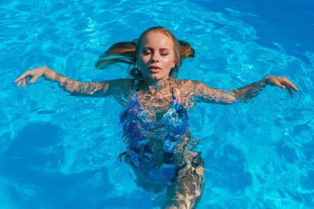 Fashion portrait of beautiful sexy young women in swimming pool outdoors. Beautiful woman swimming in a poolの写真素材