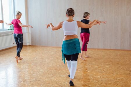 Novokuznetsk, Kemerovo region, Russia - September 07, 2019: Belly dance class. Small group of people doing belly dance exercises with teacher on class in a light room.のeditorial素材