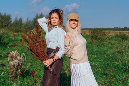 Portrait of two beautiful girls in a field in late summer. Women standing next to each other with bouquet made of dry brown plants. Concept of harmony, nature, naturalness, fashion, style, friendshipの写真素材