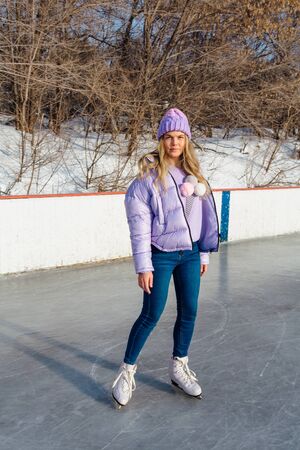 Lovely young woman riding ice skates on the ice rink. Girl skating on ice in a winter frosty day