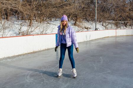 Lovely young woman riding ice skates on the ice rink. Girl skating on ice in a winter frosty day