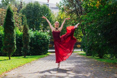 Woman ballerina in red ballet dress dancing in pointe shoes in autumn park. Ballerina standing in beautiful ballet poseの写真素材