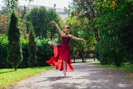 Woman ballerina in red ballet dress dancing in pointe shoes in autumn park. Ballerina standing in beautiful ballet poseの写真素材