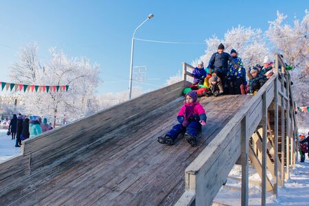 Novokuznetsk, Russia- January 07, 2019: Russian winter entertainment: children having fun tobogganing from wooden toboggan in a frosty winter dayのeditorial素材
