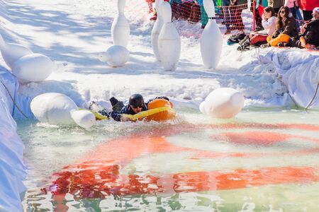 Sheregesh, Kemerovo region, Russia - April 13, 2019: Pool and ride contest where people on a swimming ring playing huge bowling on the snowy slope next to the pool with ice cold water.のeditorial素材