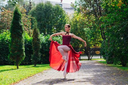 Woman ballerina in red ballet dress dancing in pointe shoes in autumn park. Ballerina standing in beautiful ballet poseの写真素材