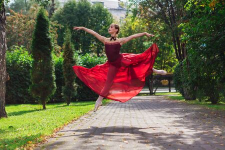 Woman ballerina in red ballet dress dancing in pointe shoes in autumn park. Ballerina standing in beautiful ballet poseの写真素材