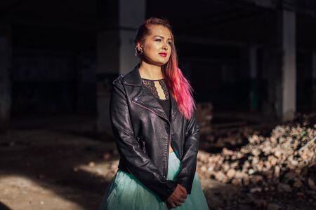 Portrait of a young girl with pink hair standing next to the bricks in a collapsed building in a...