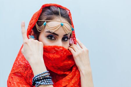 Close up portrait of a beautiful eastern woman with bright makeup and jewelry wearing red headscarf.