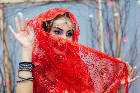 Close up portrait of a beautiful eastern woman with bright makeup and jewelry wearing red headscarf.の写真素材