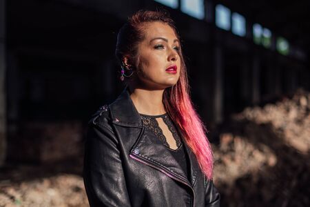 Portrait of a young girl with pink hair standing next to the bricks in a collapsed building in a...