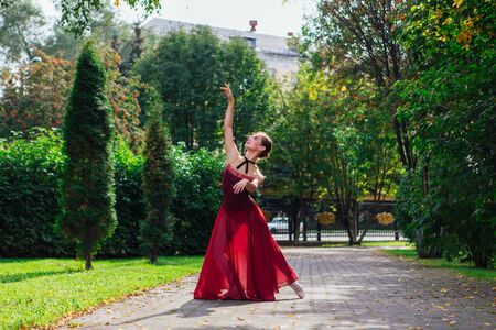 Woman ballerina in red ballet dress dancing in pointe shoes in autumn park. Ballerina standing in beautiful ballet poseの写真素材