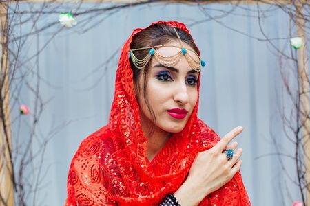Close up portrait of a beautiful eastern woman with bright makeup and jewelry wearing red headscarf.の写真素材
