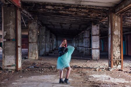 Portrait of a young girl with pink hair dressed in leather jacket and a blue skirt standing inside of collapsed building surrounded by ruinsの写真素材