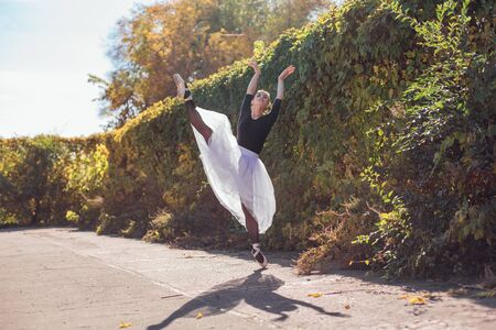 Woman ballerina in a white ballet skirt dancing in pointe shoes in a golden autumn park. Ballerina...